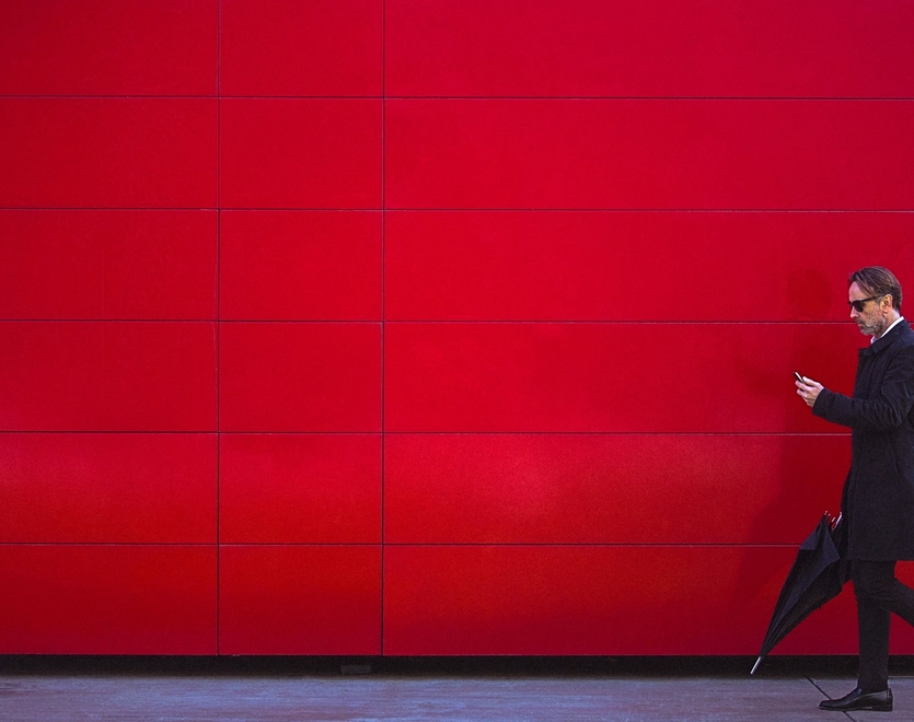 Man holding his phone at a red background.