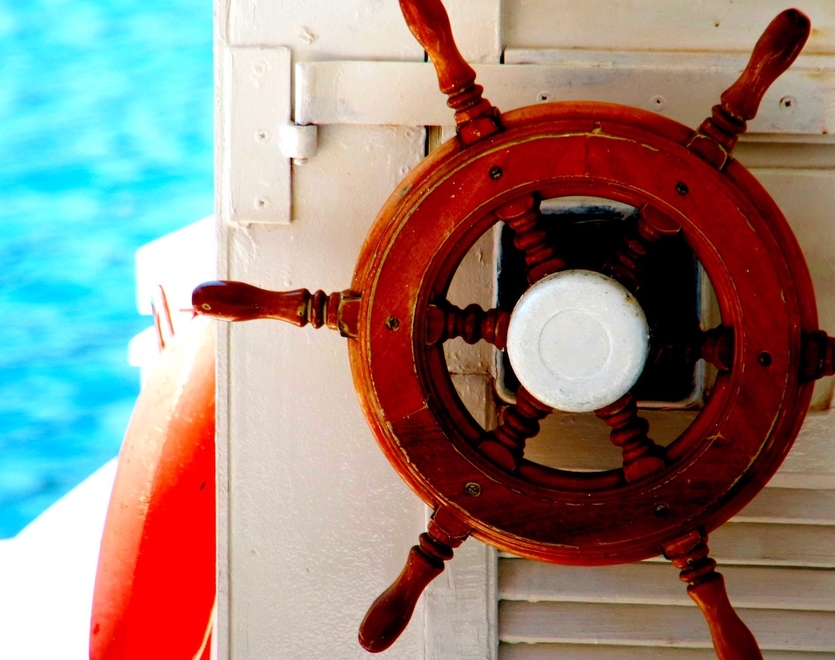 A boat's wheel, with water visible in the background.